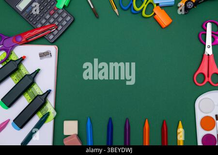 Verschiedene Schulutensilien, darunter Buntstifte, Marker, Scheren, eine Aquarellpalette und ein Taschenrechner, die auf einem grünen Hintergrund mit einem angeordnet sind Stockfoto