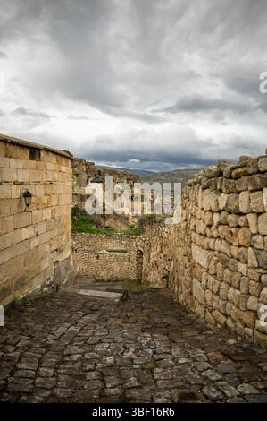 Ein Steinpfad führt zwischen Mauern in Kappadokien, Türkei, hinab und enthüllt die einzigartigen Felsformationen und Wohnungen der Region unter einem bewölkten Himmel. Stockfoto