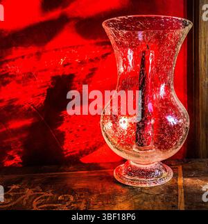 Sonnenlicht am frühen Morgen, das durch den Glaskerzenhalter auf die rot lackierte Wand scheint. Stockfoto