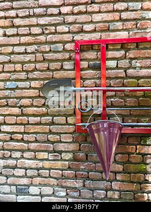 Feuerlöschwerkzeugsatz auf Ziegelwand, roter Rahmen mit Metallschaufel, Feuerhaken und konischer Eimer, Sicherheits- und Notfallausrüstung, Sicherheit am Arbeitsplatz im Freien Stockfoto