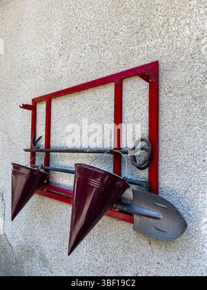 Brandbekämpfungsset an der Wand mit rotem Metallgestell, konischen Eimern, Schaufel und Haken, schräg, strukturierte Oberfläche, Sicherheits- und Notfallausrüstung. Stockfoto