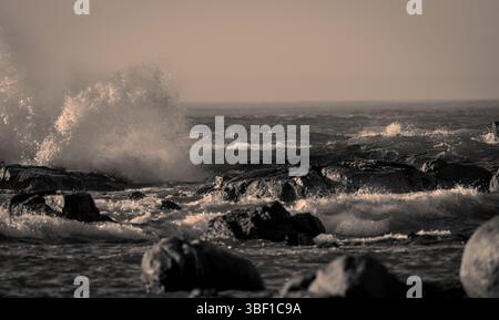 Sepia-farbenes Bild intensiver Ozeanwellen, die auf Küstenfelsen in Südafrika treffen und dramatische Wellen und Wasserbewegungen zeigen. Stockfoto