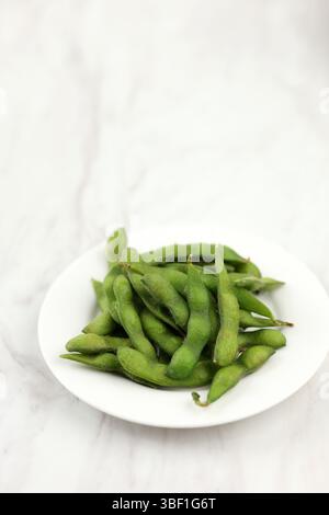 Japanische Edamambohnen, Frische Sojabohnen, Die Verzehrfertig Sind. Auf weißer Platte, weißer Tisch Stockfoto