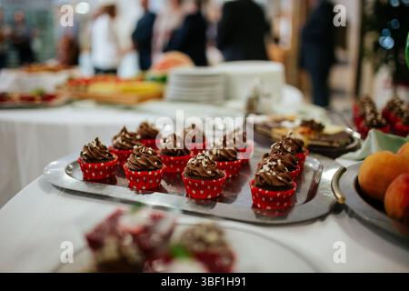 Ein Nahaufnahme-Foto von mehreren Schokoladen-Cupcakes auf einem goldfarbenen Tablett. Die Cupcakes werden mit einer reichhaltigen Schokoladenbuttercreme übergossen und garniert Stockfoto