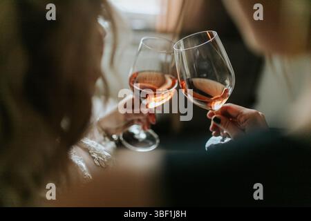 Eine Nahaufnahme von zwei Freunden, die mit Gläsern Roséwein tosten. Das Bild fängt den intimen Moment der Feier mit sanfter, natürlicher Beleuchtung ein Stockfoto