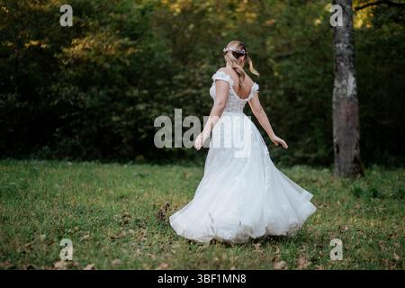 Das Bild zeigt eine Braut in einem eleganten weißen Hochzeitskleid in einer ruhigen Waldumgebung. Das Kleid ist mit zarten Spitzendetails versehen Stockfoto