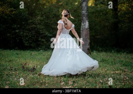 Das Bild zeigt eine Braut in einem eleganten weißen Hochzeitskleid in einer ruhigen Waldumgebung. Das Kleid ist mit zarten Spitzendetails versehen Stockfoto