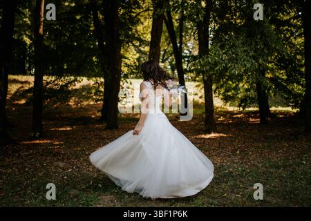 Das Bild zeigt eine Braut in einem eleganten weißen Hochzeitskleid in einer ruhigen Waldumgebung. Das Kleid ist mit zarten Spitzendetails versehen Stockfoto