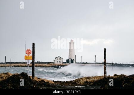 Weißer Leuchtturm, der stark gegen abstürzende Wellen in island steht Stockfoto