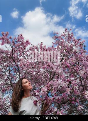 Frau, die im Frühjahr vor dem blühenden Magnolienbaum steht. Stockfoto