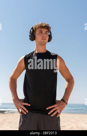 Junger Athlet mit Kopfhörern, die den Himmel am Strand beobachten Stockfoto