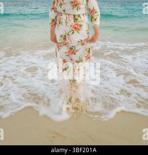 Frau im Blumenkleid, die in sanften Meereswellen steht Stockfoto
