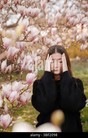 Junge Frau mit Kopfschmerzen in der Nähe blühender Magnolienbäume Stockfoto
