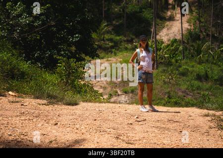 Eine Frau, die selbstbewusst auf einem unbefestigten Pfad im tropischen Dschungel steht Stockfoto