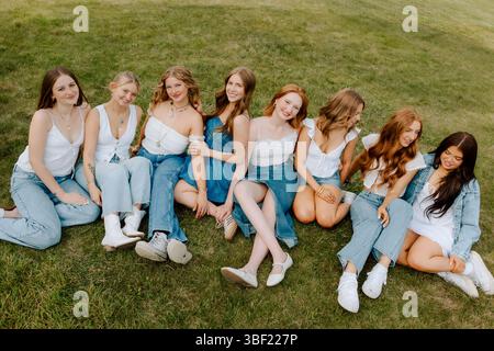 Universitätsstudenten tragen Denim- und weiße Outfits, die sich auf dem Gras entspannen Stockfoto