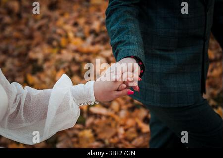Eine Nahaufnahme zeigt ein Paar, das Hand in Hand durch einen dichten Herbstwald geht, der mit lebhaften, gefallenen Blättern bedeckt ist, und zeigt eine romantische Verbindung Stockfoto