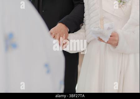 Eine Nahaufnahme einer Hochzeitszeremonie zeigt einen Bräutigam in einem dunklen Anzug und eine Braut in einem weißen Kleid, deren Hände zusammengeschlossen sind und die Liebe symbolisieren Stockfoto