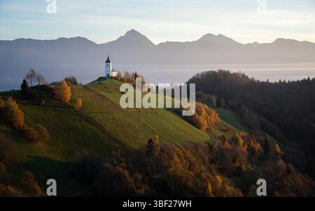 Malerische Alpenlandschaft mit einer kleinen Kirche auf einem Hügel und Bergen im Hintergrund, Slowenien Stockfoto