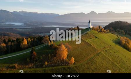 Malerische Alpenlandschaft mit einer kleinen Kirche auf einem Hügel und Bergen im Hintergrund, Slowenien Stockfoto