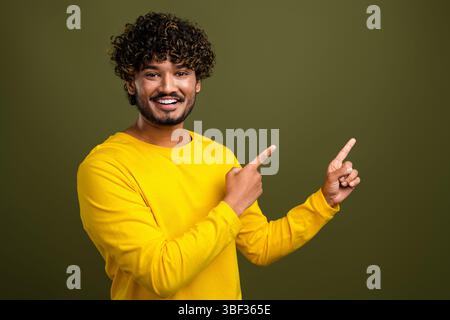 Fröhlicher junger Mann in einem gelben Hemd, der Gesten vor khakifarbenem Hintergrund macht Stockfoto