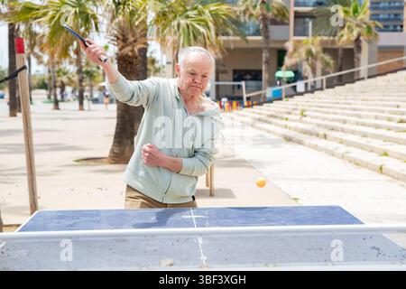 Pensionierter Mann, der Tischtennis auf dem Straßentisch spielt Stockfoto