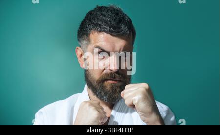 Karate-Mann in Kampfstellung. Männliche Karatekämpfer üben Schläge während des Karatetrainings. Bärtiger Mann in weißem Kimono mit geballten Händen in der Faust Stockfoto