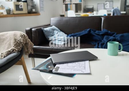 Wohnzimmer mit komfortabler Couch mit Kissen, Notizbuch und Dokumenten auf Couchtisch und gemütlicher Atmosphäre. Das Zimmer bietet eine Mischung aus ungezwungener und organisierter Atmosphäre Stockfoto
