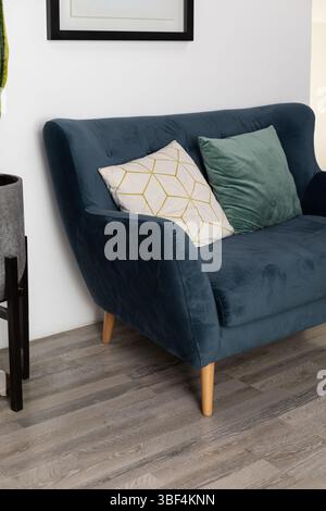 Ein stilvolles blaues Sofa mit natürlichen Holzbeinen in einem hellen, modernen Wohnbereich. Dieses Bild zeigt Komfort und modernes Innendesign, per Stockfoto