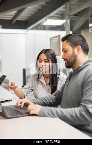 Eine junge Frau und ein Mann stehen Seite an Seite, betrachten einen Laptop-Bildschirm und diskutieren Daten. Die Büroumgebung spiegelt Teamarbeit, Kommunikation und ein wider Stockfoto