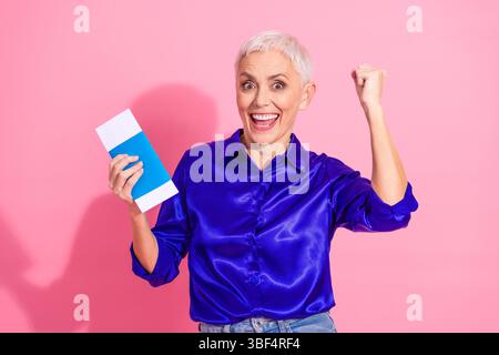 Fröhliche reife Frau in blauem Hemd, die einen Umschlag mit rosafarbenem Hintergrund hält Stockfoto