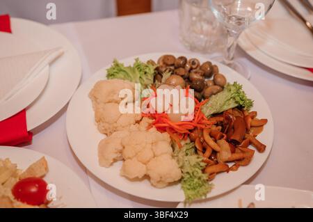 Ein wunderschön angelegter Vorspeiseteller enthält verschiedene Pilzsorten, Blumenkohl, Karotten und eingelegte Zwiebeln, präsentiert auf einem knusprigen weißen Tisch Stockfoto