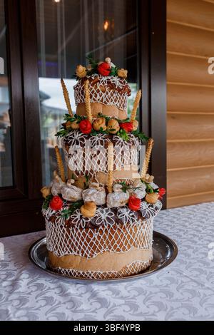 Eine atemberaubende dreistufige ukrainische Korovai-Hochzeitstorte mit komplizierter Glasur, verziert mit Haselnüssen und roten Früchten, die Wohlstand und f symbolisieren Stockfoto