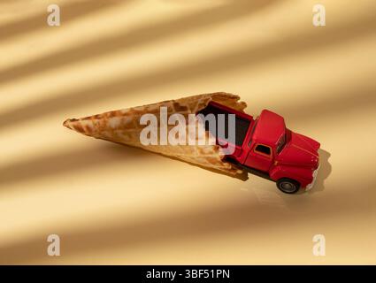 Roter Spielzeugwagen kommt aus einer Eiskugel. Minimalistisches Transportkonzept Stockfoto