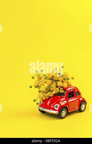 Moskau, Russland - 23. Februar, 8. März 2019: Internationaler Tag der Frau Karte mit Spielzeug Modell der retro Auto Lieferung Blumenstrauß von Mimosa Blumen auf Gelb Stockfoto