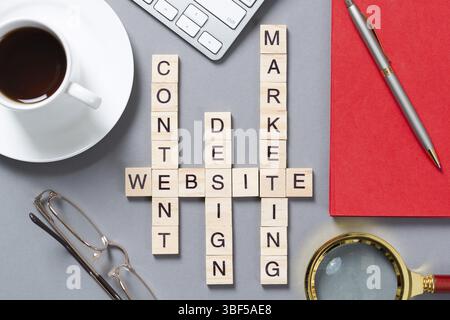 Web-Marketing-Konzept mit Wörtern aus Cubes. Stillleben des Büroarbeitsplatzes mit Kreuzworträtsel. Flache graue Oberfläche mit pc-Tastatur und Tasse Kaffee. Stockfoto