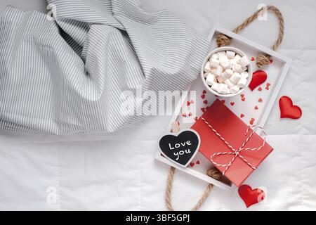 Kreative, oben flach sill Leben romantischen Komposition. Heißer Kakao Kaffee Schokolade mit Marshmallows Becher rot Geschenk herzen Fach im Bett. Konzept Valen Stockfoto