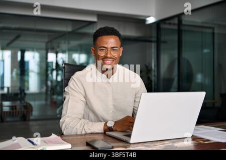 Glücklicher professioneller afrikanischer Geschäftsmann, der bei der Arbeit auf die Kamera schaut, Porträt. Stockfoto