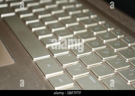 Eine goldfarbene Tastatur eines Laptops mit verschwommenem Hintergrund in hellem Licht auf einer Oberfläche. Stockfoto