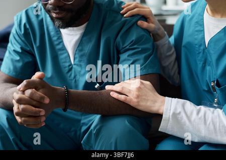 Medizinisches Fachpersonal, das Gespräche führt, während es den Behandlungsplan überprüft, Peelings trägt und drinnen sitzt. Schwarze Person in medizinischer Kleidung, die an der Diskussion teilnimmt Stockfoto