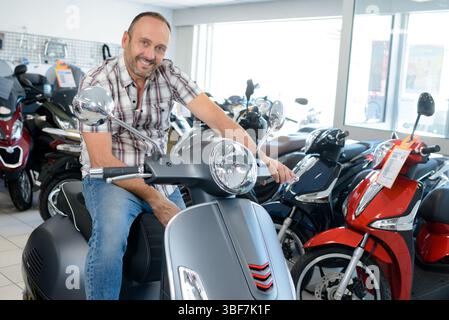 Der Mann saß auf einem modernen Roller in einem Verkaufsraum des Händlers Stockfoto