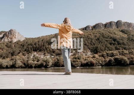 Frau in gelber Jacke, die den Blick auf Berge und See genießt Stockfoto