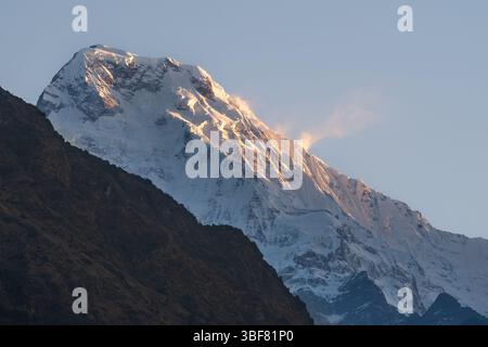 Ein atemberaubender Blick auf den schneebedeckten Gipfel von Annapurna South, wenn die Wolken sanft die Berge im großen Himalaya in Nepal umarmen. Stockfoto