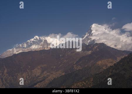 Ein atemberaubender Blick auf die schneebedeckten Gipfel von Annapurna I. und Annapurna South, wenn die Wolken sanft die Berge im großen Himalaya in Nepal umarmen. Stockfoto