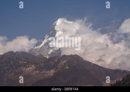 Ein atemberaubender Blick auf den schneebedeckten Gipfel von Annapurna South, wenn die Wolken sanft die Berge im großen Himalaya in Nepal umarmen. Stockfoto