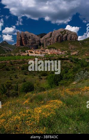 Das Dorf Agüero in den Pyrenäen in der Provinz Huesca, Aragon, Spanien, ist um den Turm der mittelalterlichen Kirche gruppiert, der von den Syncline Hills oder Los Mallos de Agüero (den Mallets oder Ninepins von Agüero) gezehrt wird. Spektakuläre Formation des rötlichen Konglomeratgesteins aus der Tertiärzeit, geformt durch Wind- und Wassererosion, erhebt sich bis zu 275 m oder 900 Fuß über der Siedlung. Stockfoto