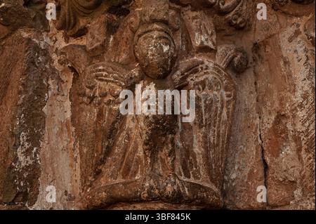 Birdman mit menschlichem Gesicht und talonierten Füßen auf der spanischen romanischen Nordtür der 1100er Jahre, die dem Meister von Agüero von Iglesia de San Salvador in Agüero, Provinz Huesca, Aragon, Spanien zugeschrieben wird. Die Kapitelle, das reich geschnitzte Tympanon und die dekorierten Archivolte darüber enthalten Flecken und Fragmente seltener, uralter mehrfarbiger Farben. Stockfoto