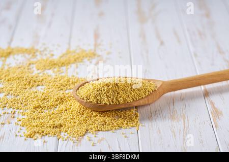 Gelbe Hirsekörner bröckeln von einem Holzlöffel auf einem Leuchttisch, selektiv fokussiert. Stockfoto