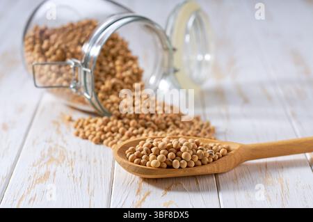 Bio-Sojabohnen in Holzschaufel und im Vorratsglas aus Glas auf einem Leuchttisch, selektiver Fokus. Stockfoto
