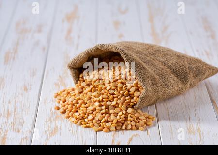 Trockene gelbe Erbsen im Sackbeutel. Sack mit organischen trockenen gelben Erbsen. Organische gelbe Erbsen in Sackleinen und Erbsenhaufen. Stockfoto