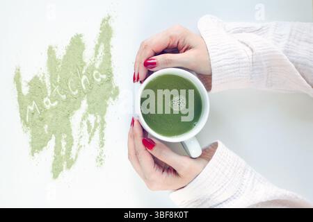 matcha Latte in einer weißen Tasse in den Händen einer Frau. Tasse Matcha Stockfoto